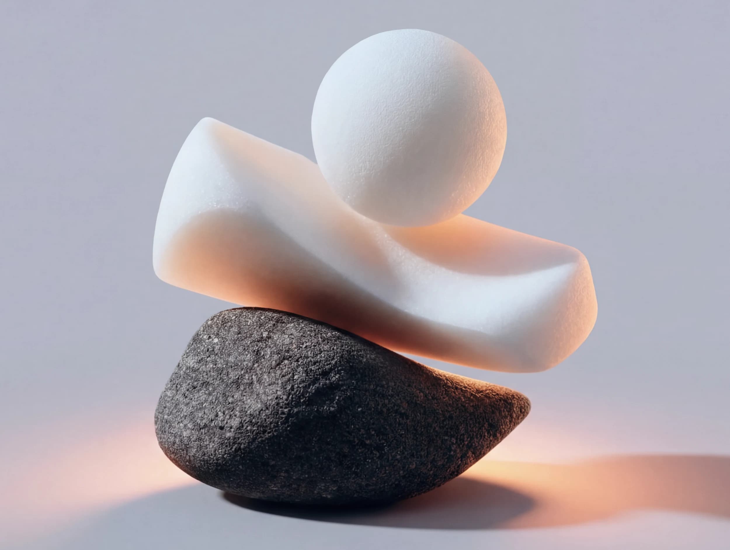 A white sphere resting on a curved white form balanced over a dark stone, lit warm from below
